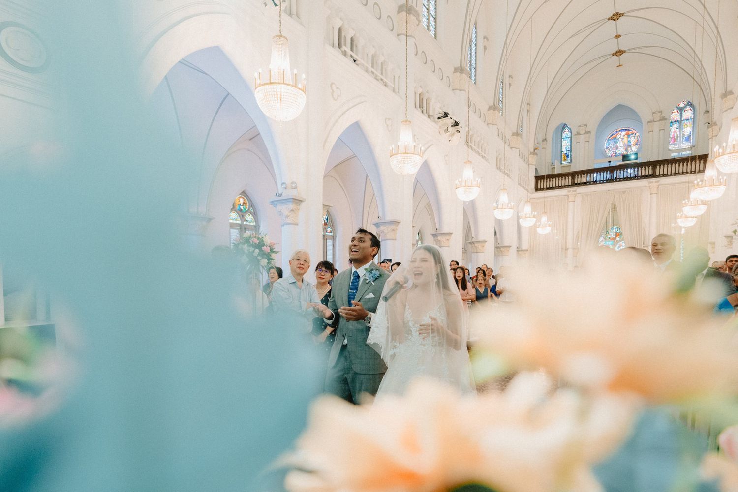 Elegant church wedding ceremony with couple at altar, surrounded by floral arrangements and stunning white arched architecture.