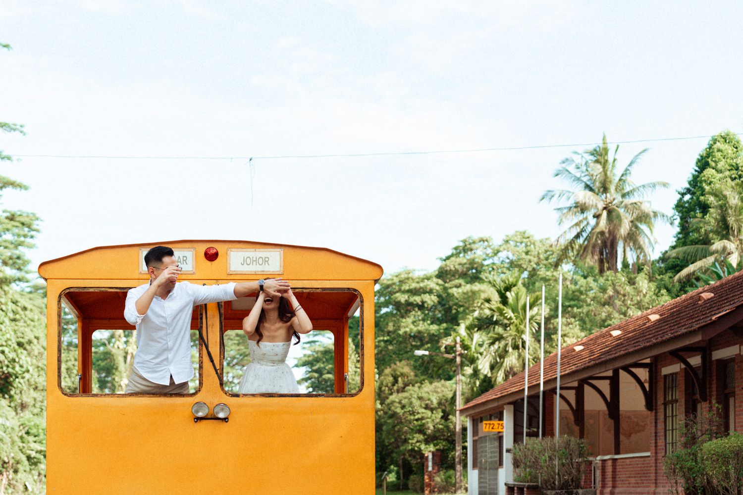 Couple in white outfits posing together in a romantic outdoor photoshoot with a bright orange train car.