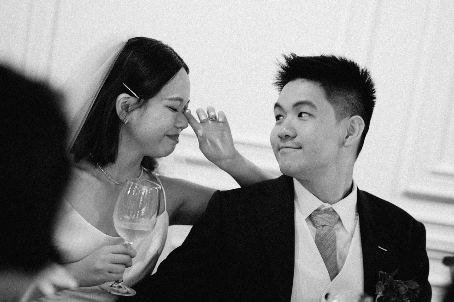A candid black and white wedding reception photo capturing a couple sharing a joyful moment with wine glasses.