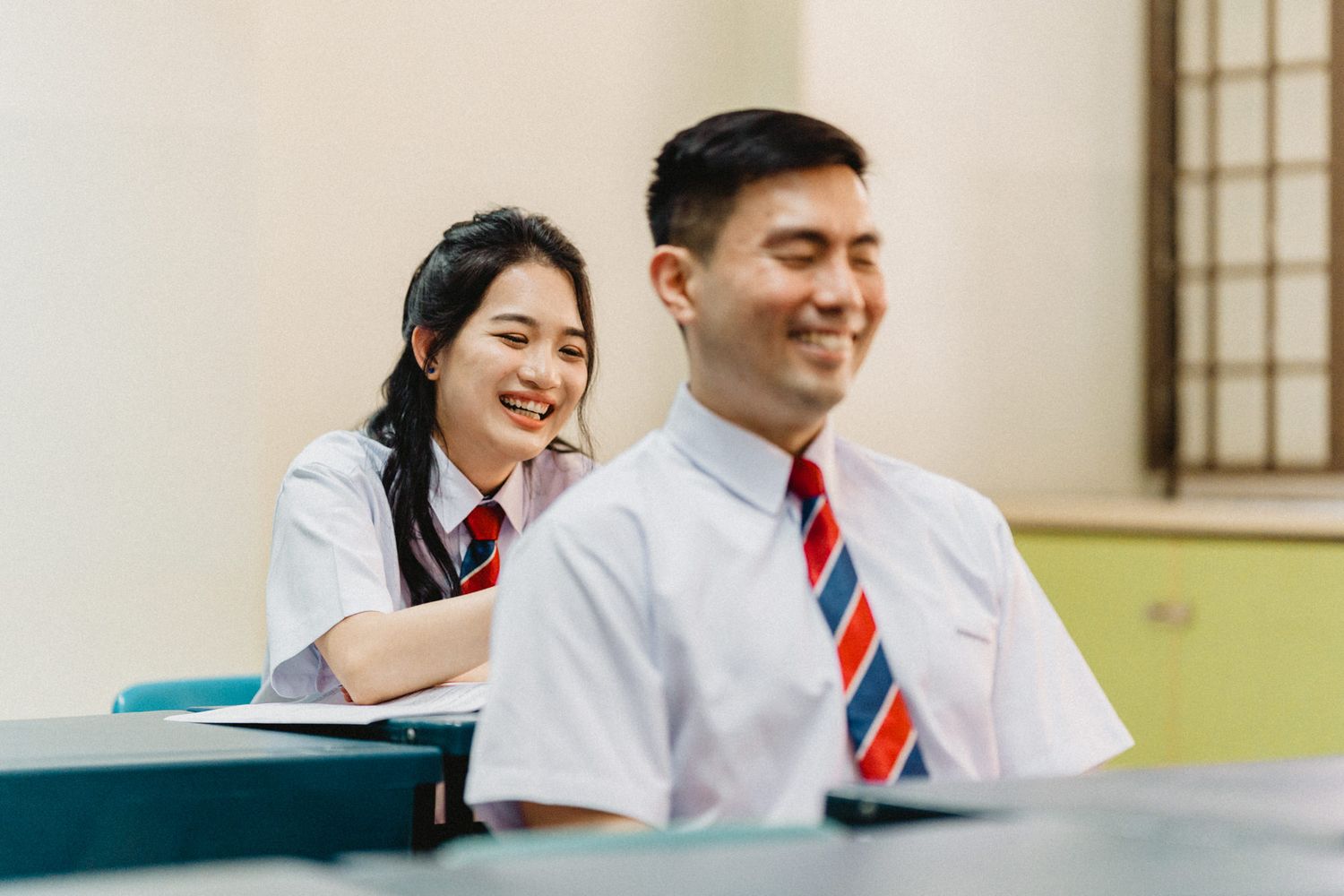 Students in white uniforms and ties sharing a joyful moment while studying together.