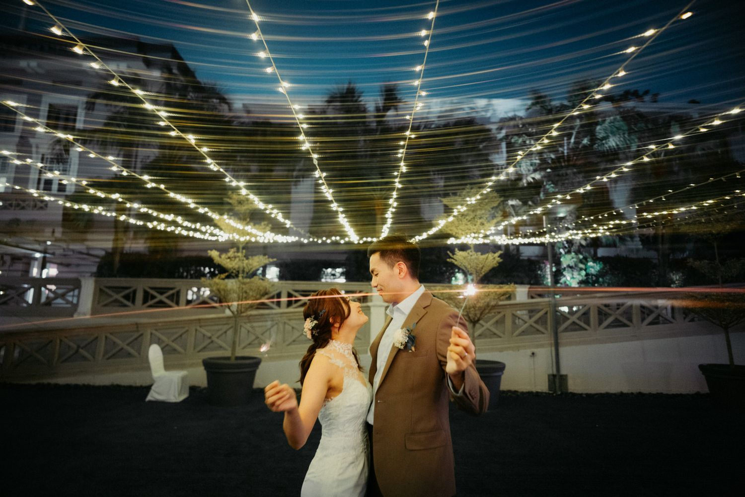 Bride and groom share romantic first dance under glowing string lights at elegant outdoor wedding reception at night.