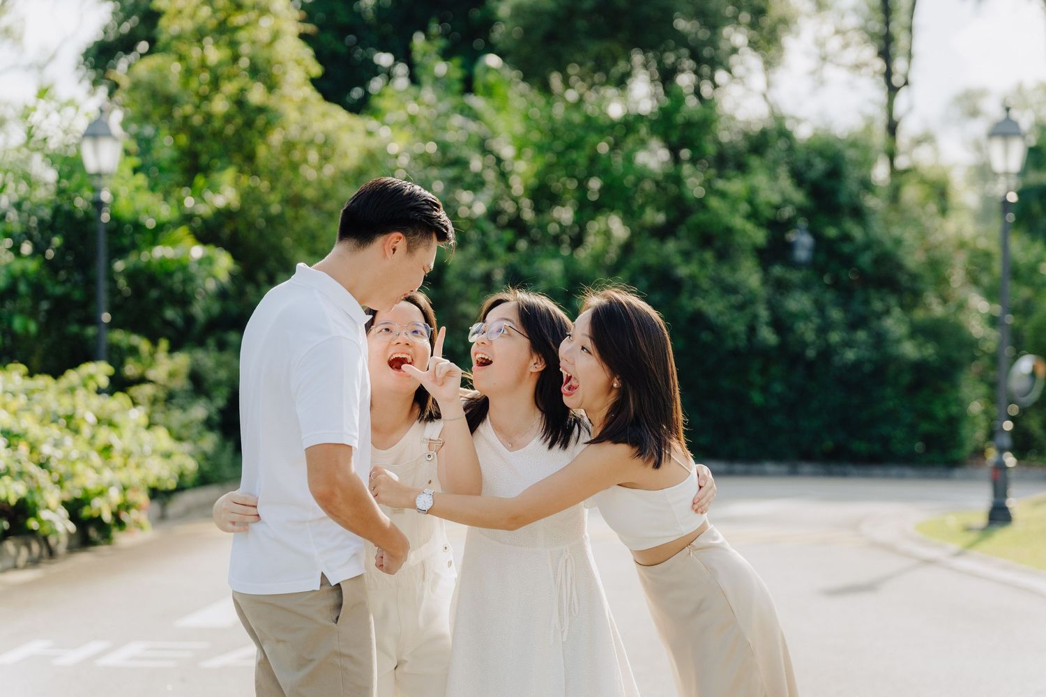 A group in white outfits walks and laughs together in a sunny garden setting during a photoshoot.