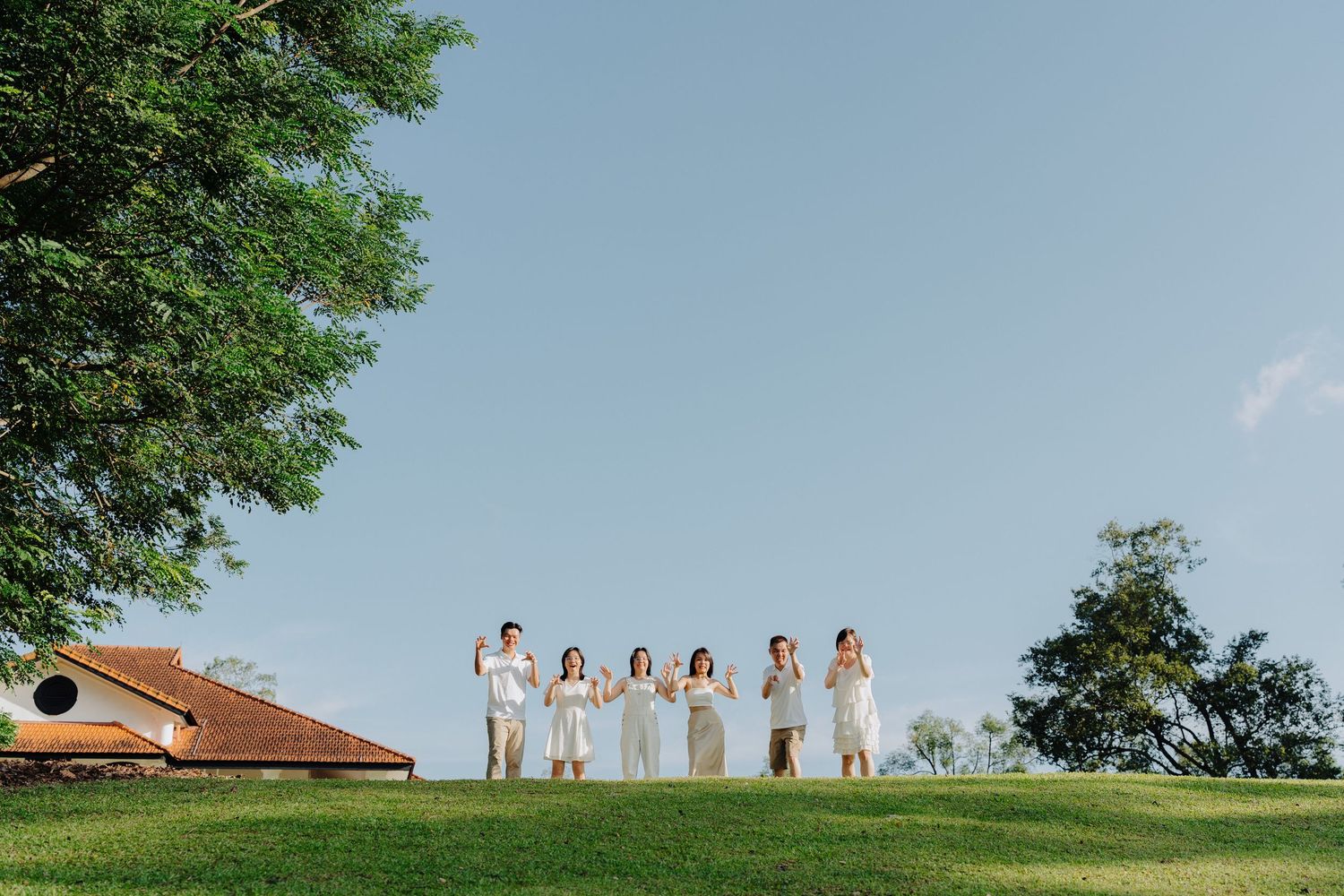 A group of people in white dresses stand together on a grassy hilltop against a blue summer sky.