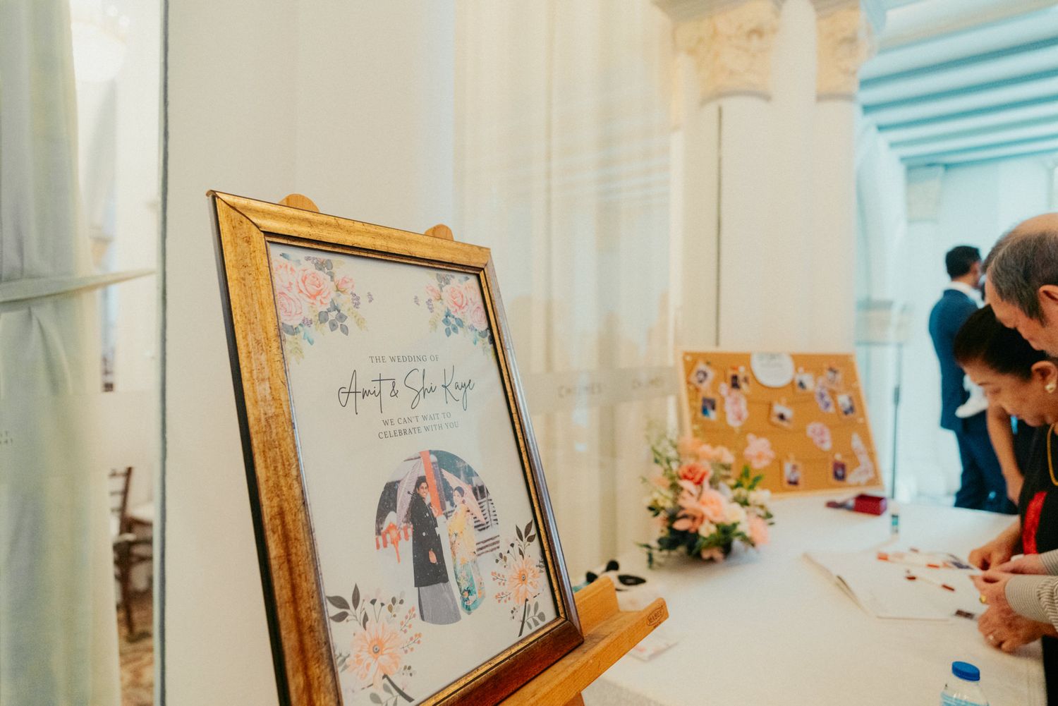Elegant wedding guest book display with illustrated portrait in gold frame and floral decorations.