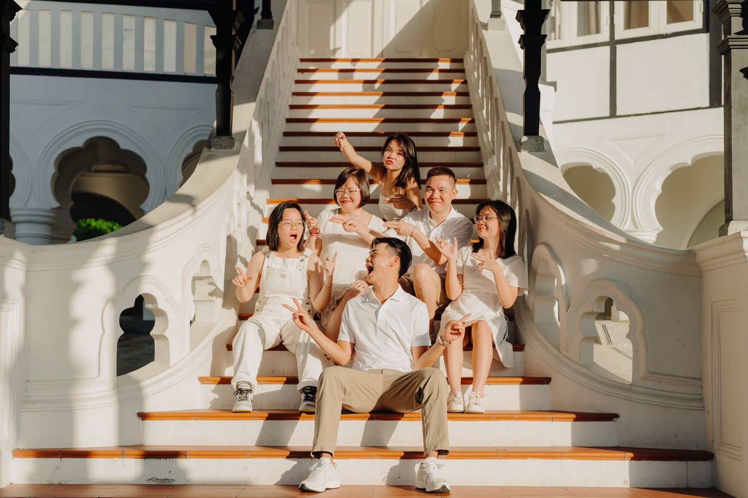 A group in white outfits sits together on an elegant staircase for a formal photo session.