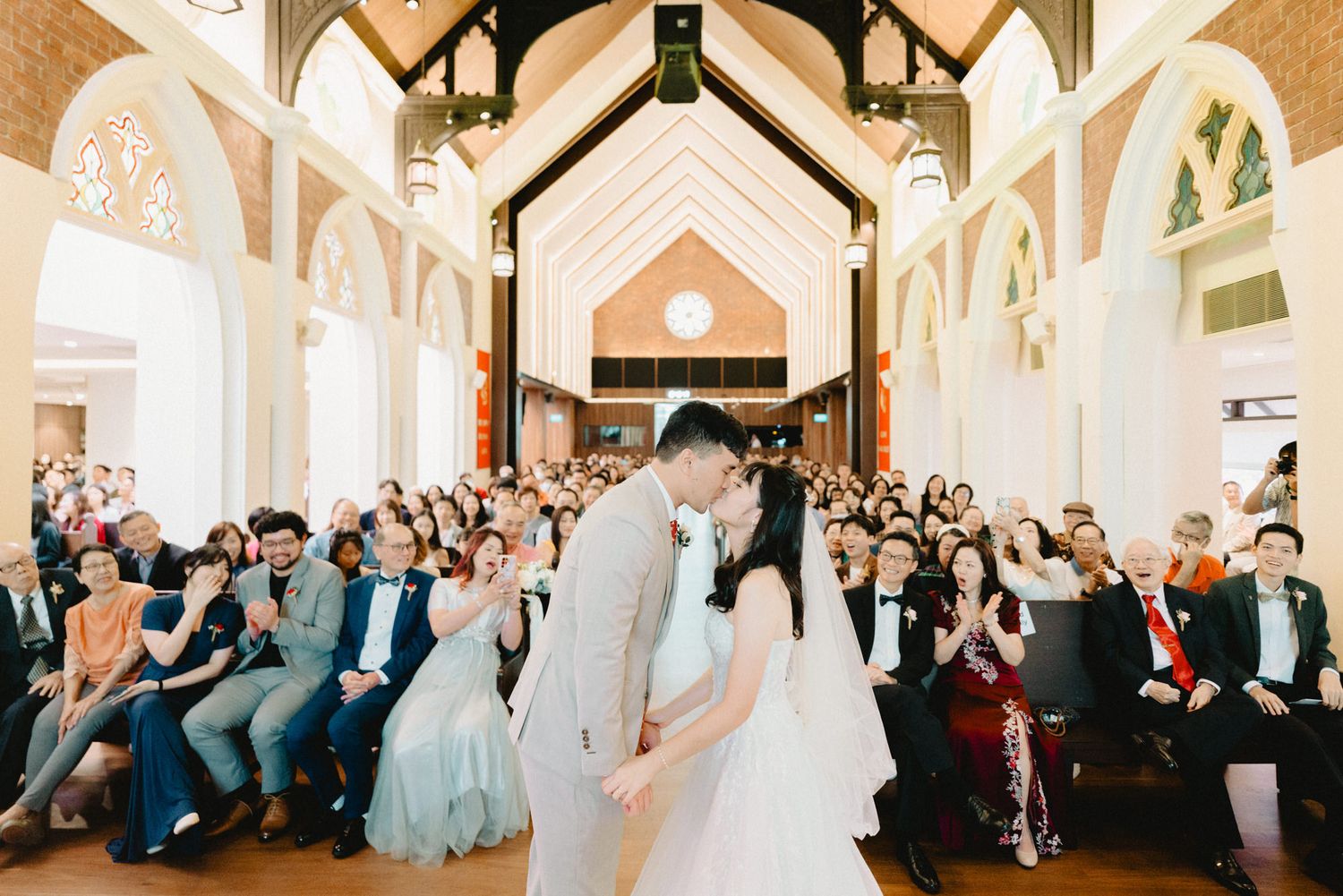Bride and groom share a kiss at the altar in an elegant chapel filled with wedding guests during a romantic ceremony.