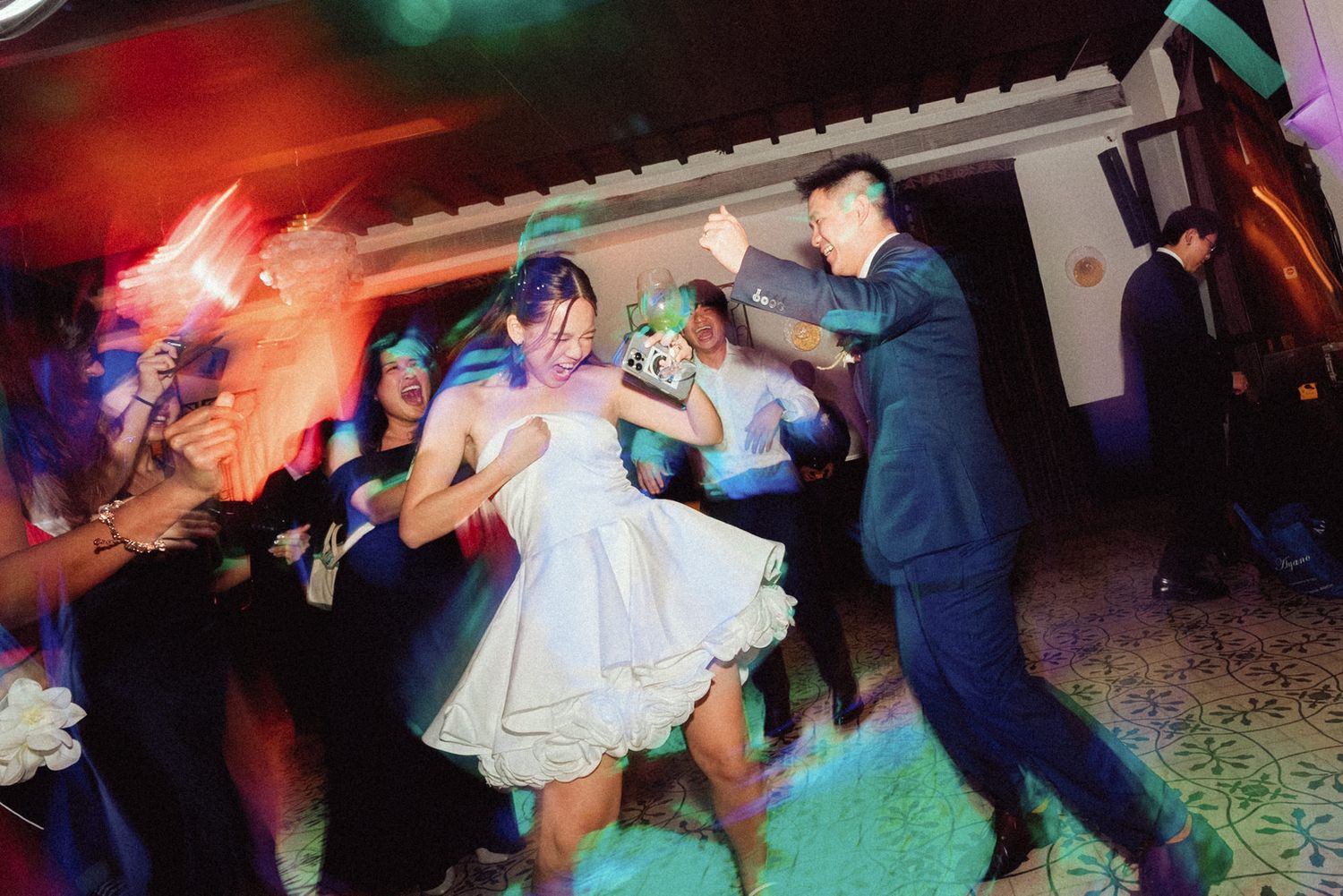 Wedding guests dancing in a colorful reception venue with vibrant red and blue lighting effects.