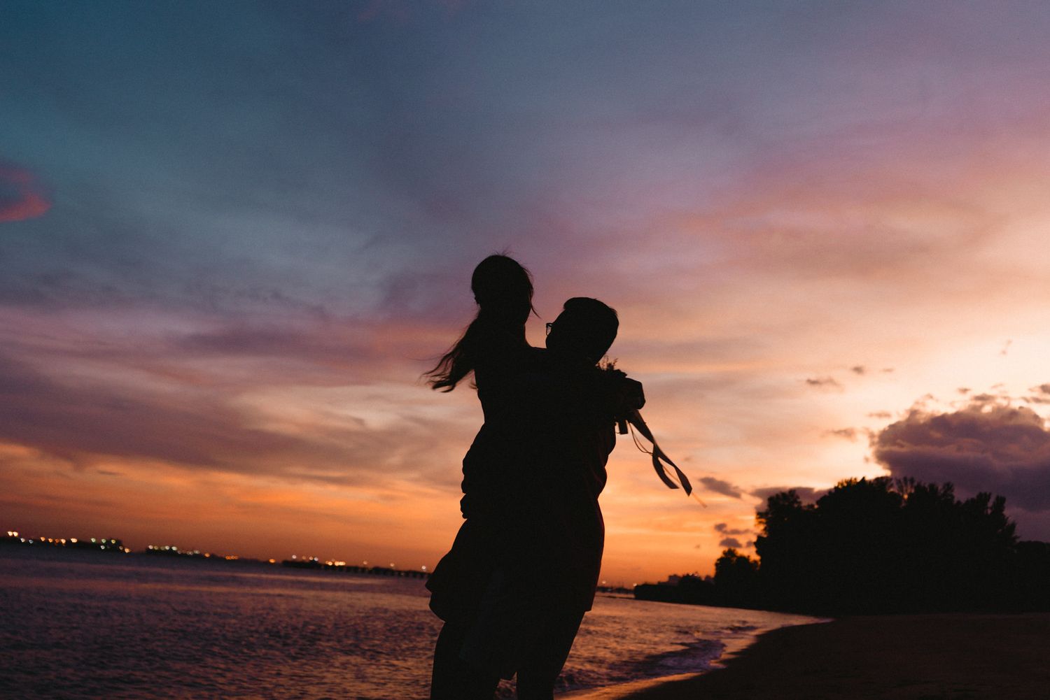 Silhouettes of a couple against a dramatic sunset sky by the ocean.
