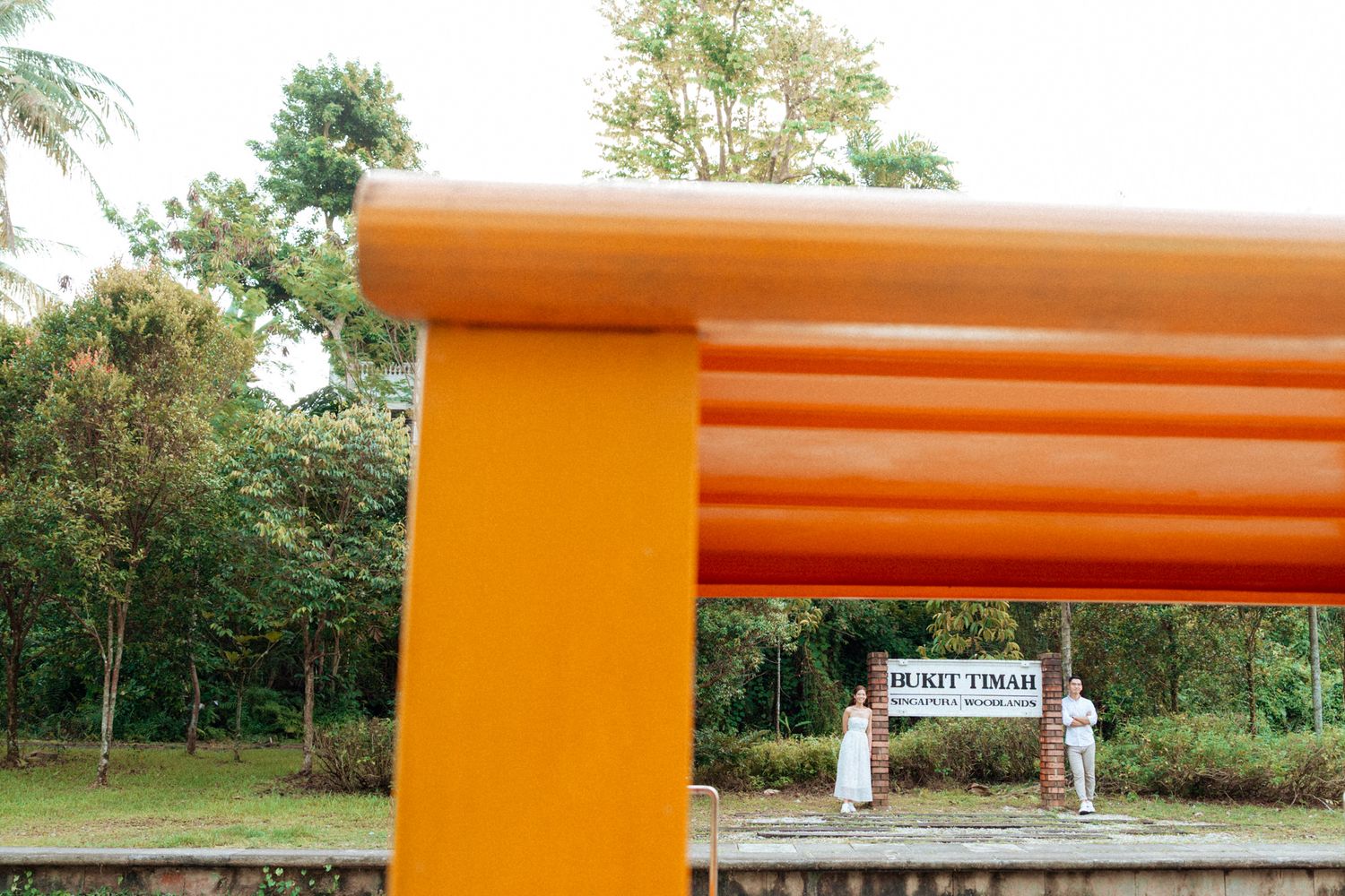 Orange archway structure with trees and foliage in the background at sunset.