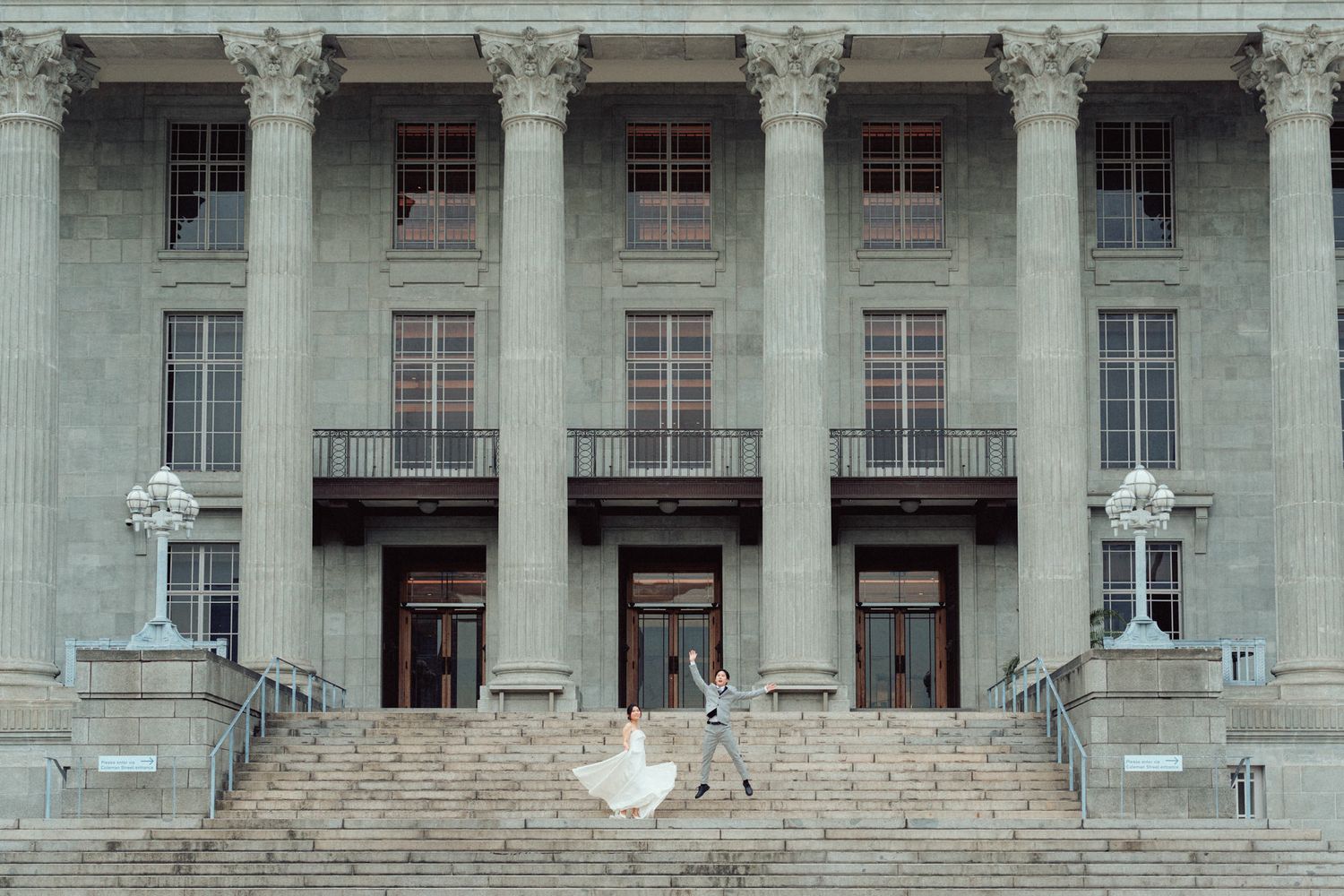 Couple dancing on grand stone steps of a neoclassical building with tall columns during their wedding day.