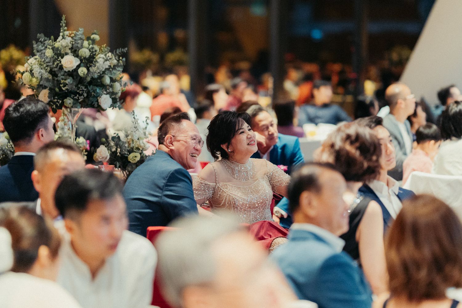 Guests laughing and celebrating at a wedding reception banquet, dressed in formal attire.