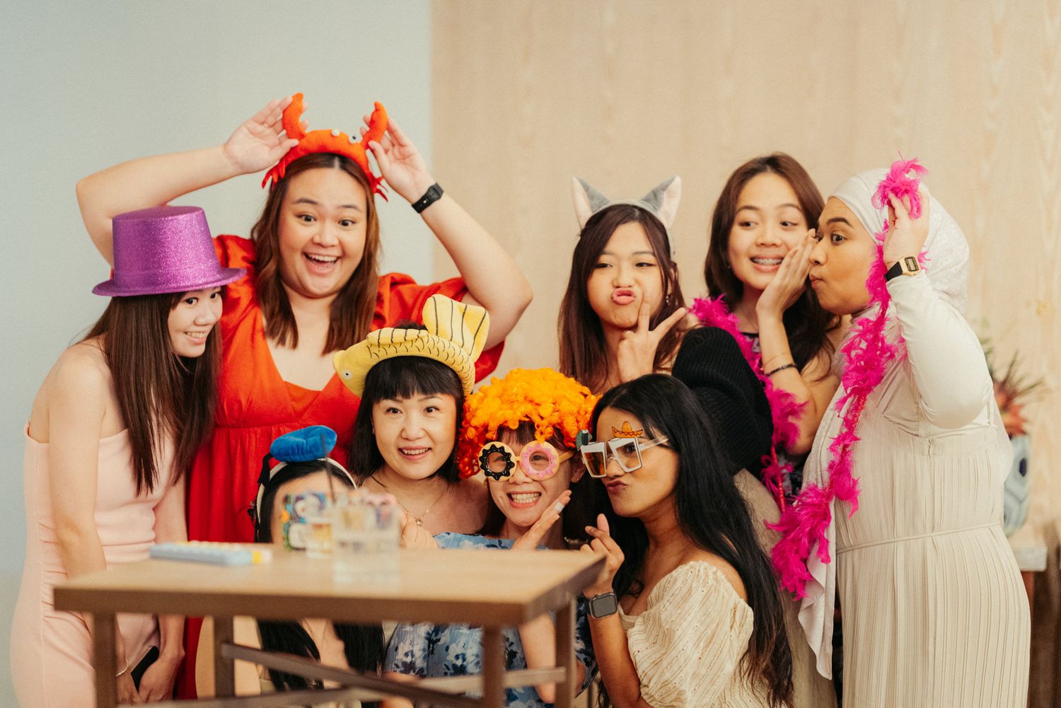 Group of young women posing with colorful party props including hats, boas, and fun accessories at a festive celebration.