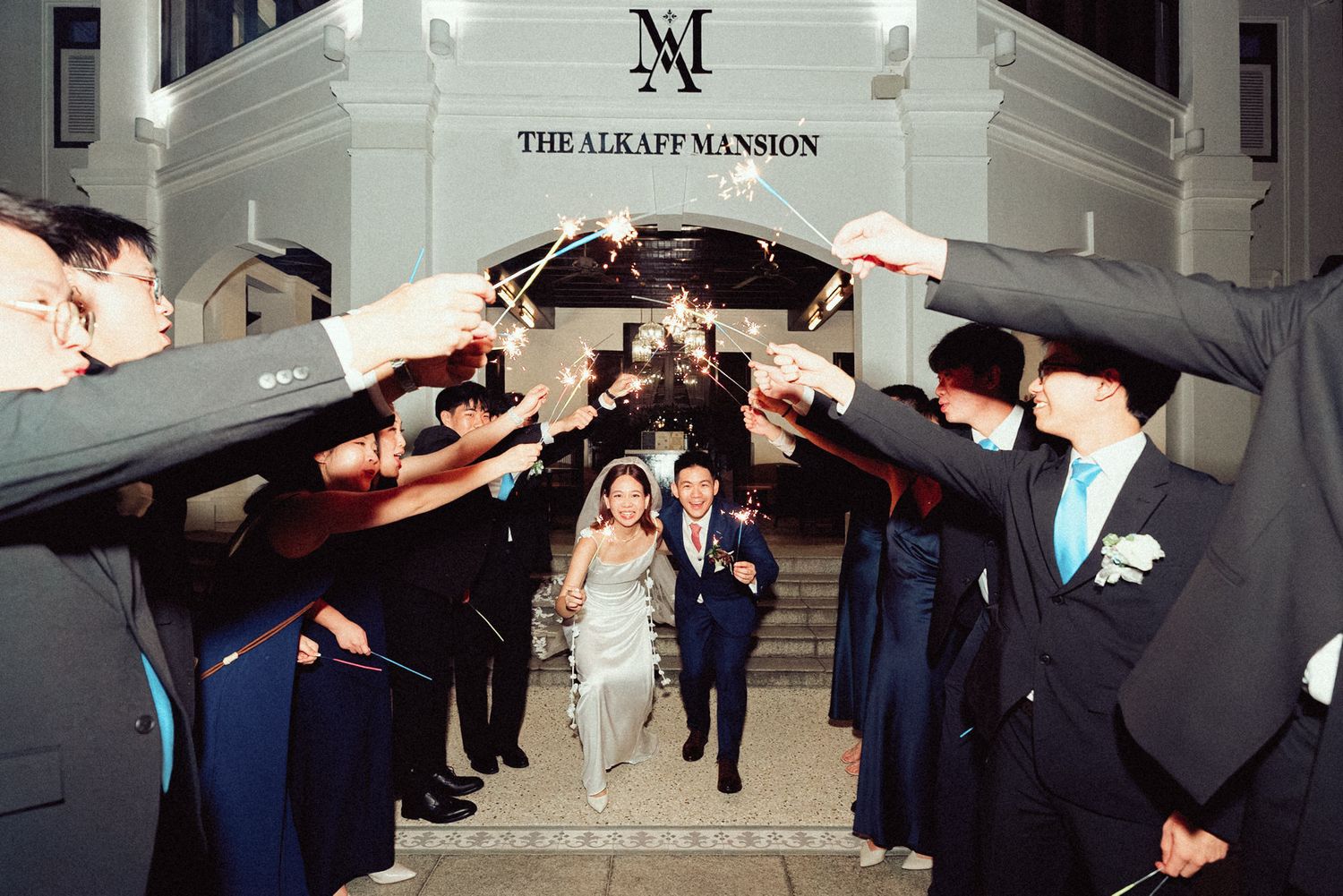 Wedding guests form an arch with sparklers as a couple walks through during a nighttime celebration at the Lucas Mansion.