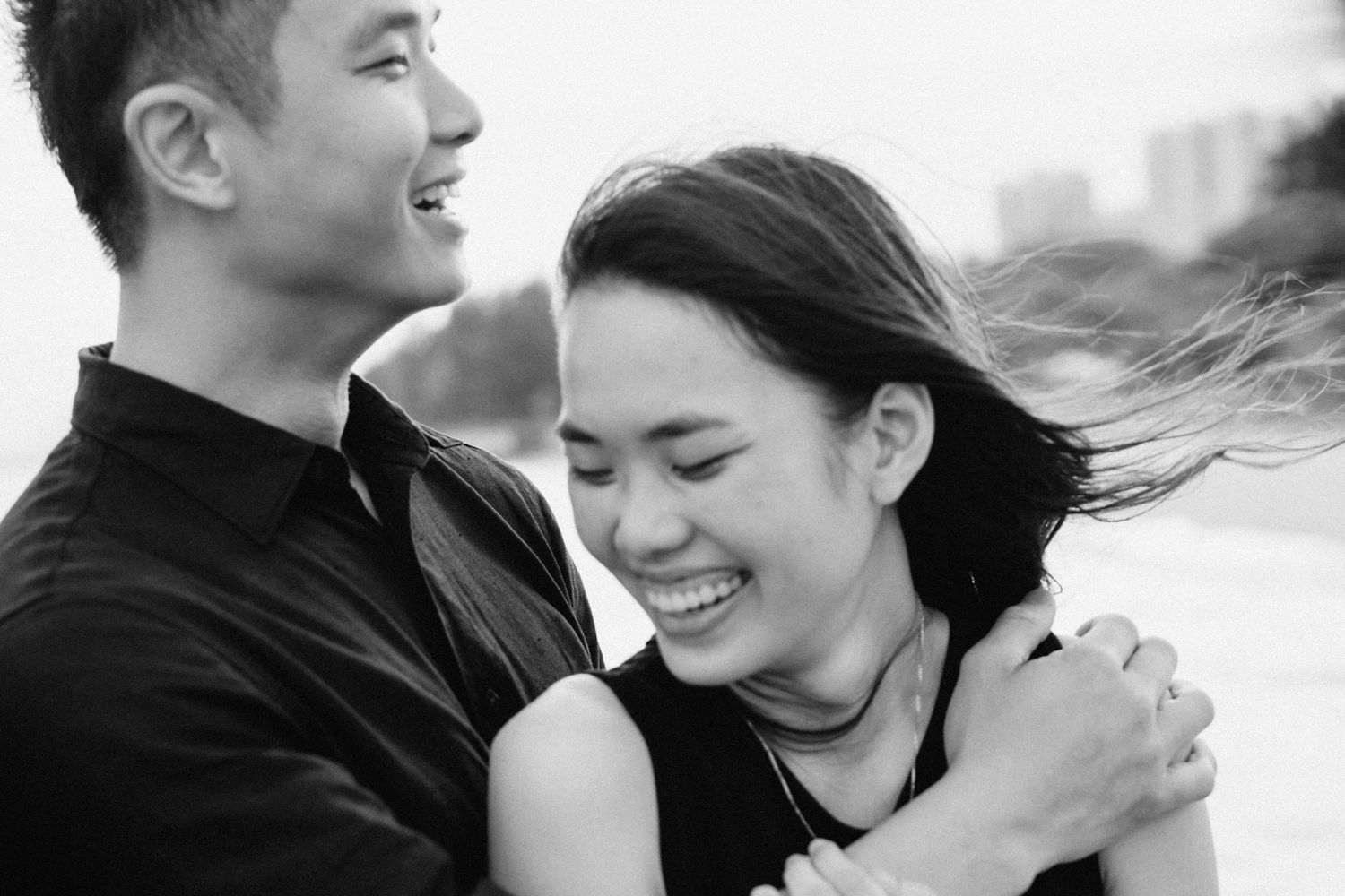 Joyful couple sharing candid moments of laughter on a cloudy beach day.
