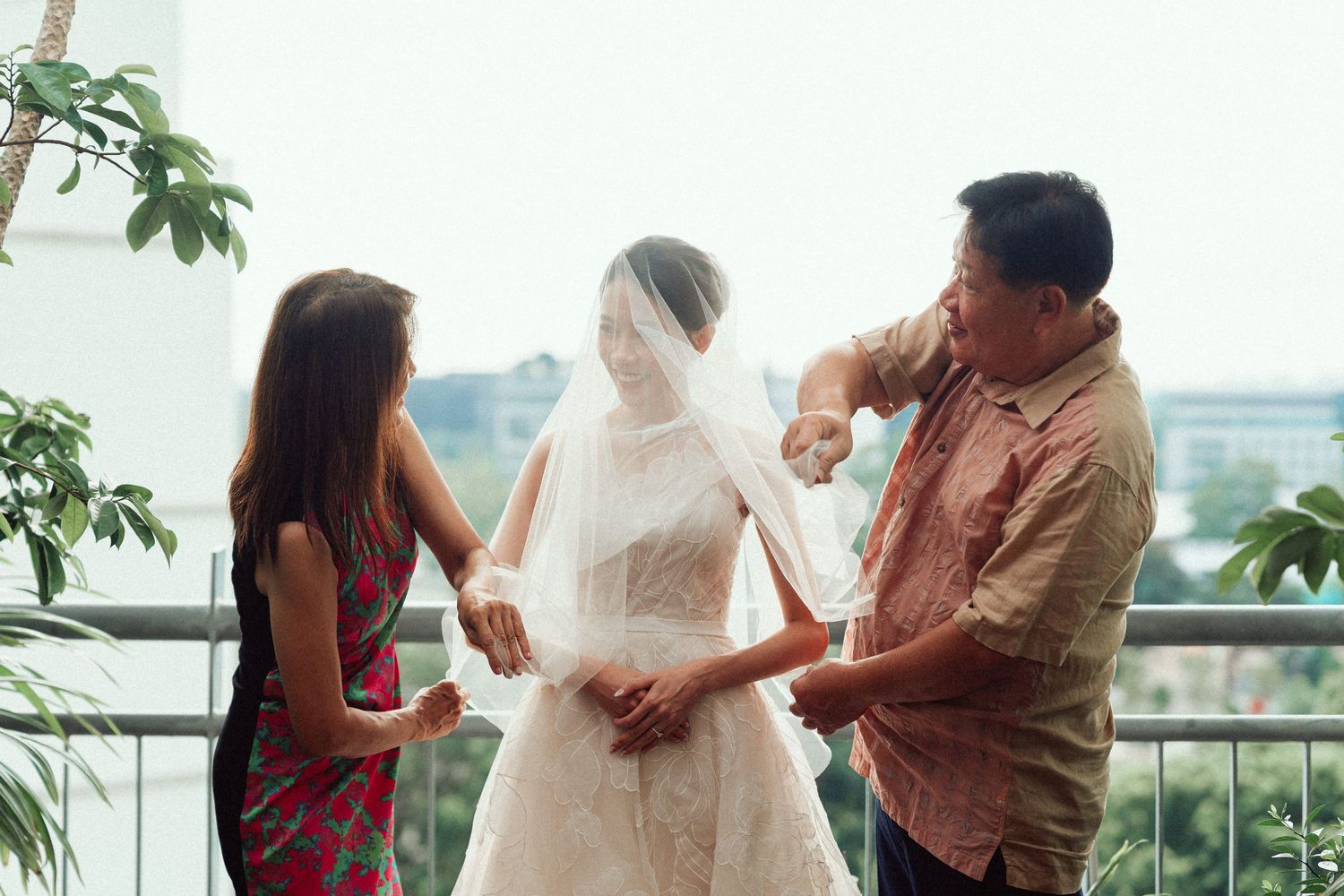Wedding preparation scene on a balcony with people helping with a bridal veil.