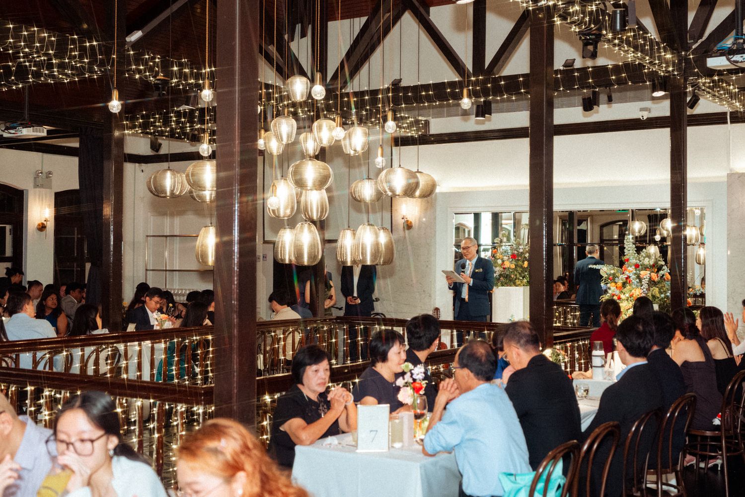 Elegant restaurant dining room with globe pendant lights, fairy lights, and guests seated at white-clothed tables.