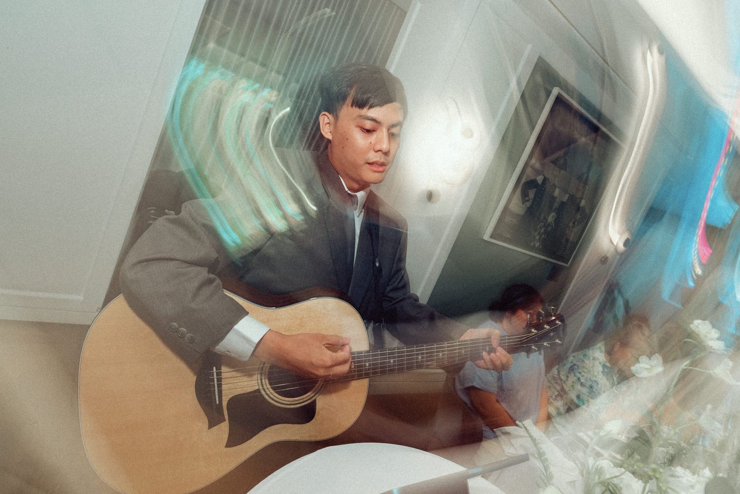 A musician plays acoustic guitar in a room with artistic lighting effects.