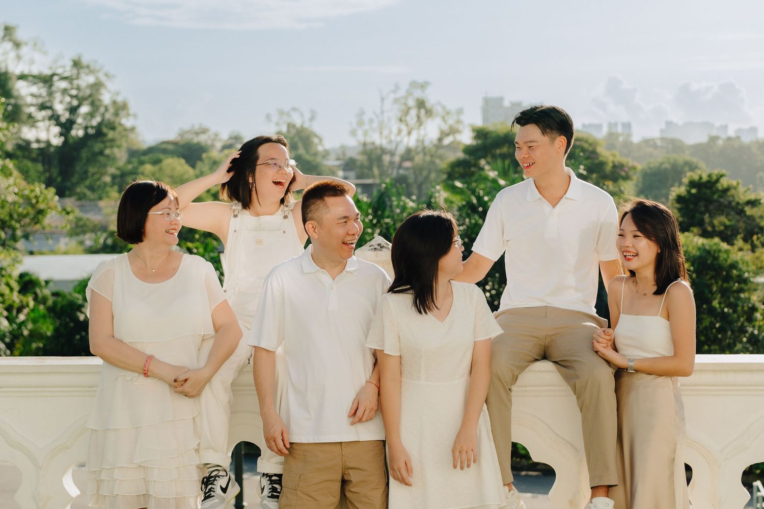 Wedding party in neutral colored outfits laughing and embracing together on a sunny outdoor terrace.