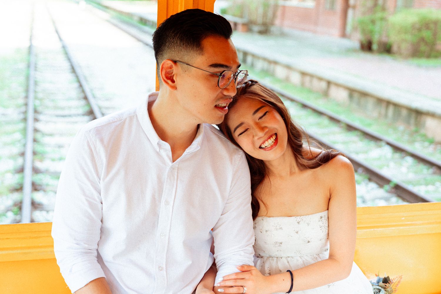 Couple sharing a romantic moment on vintage railway tracks beside an orange rail car.