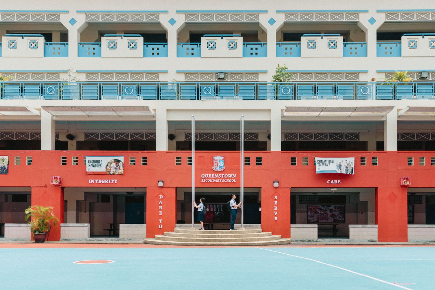 Long horizontal view of a school building with blue windows and orange-painted walls.