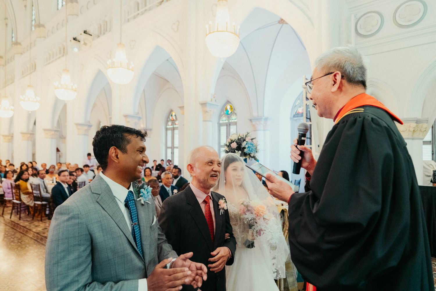 Wedding ceremony in elegant church with groom, officiant, and guests in background.