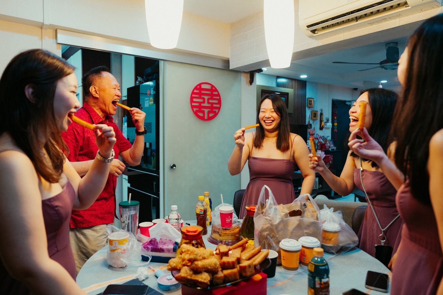 Group of friends enjoying a festive Chinese celebration dinner, laughing and sharing food around a table.