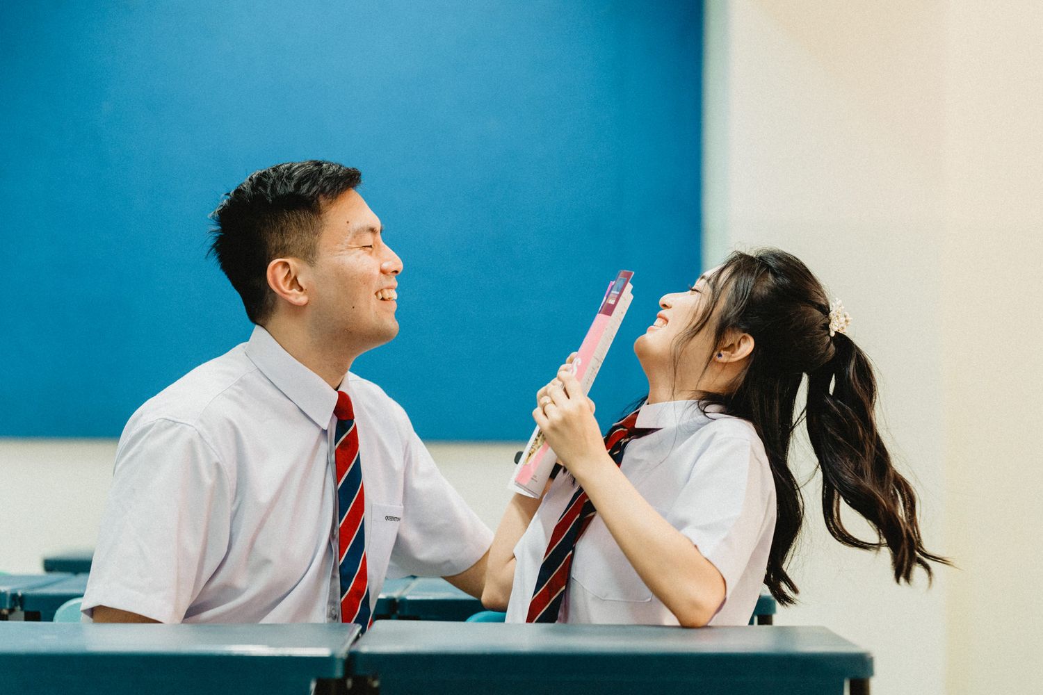 Students in white uniforms interacting playfully in a classroom with blue accent walls.