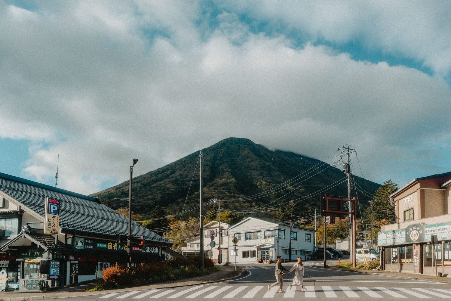 A scenic Japanese street view with mountains and cloudy skies in the background.