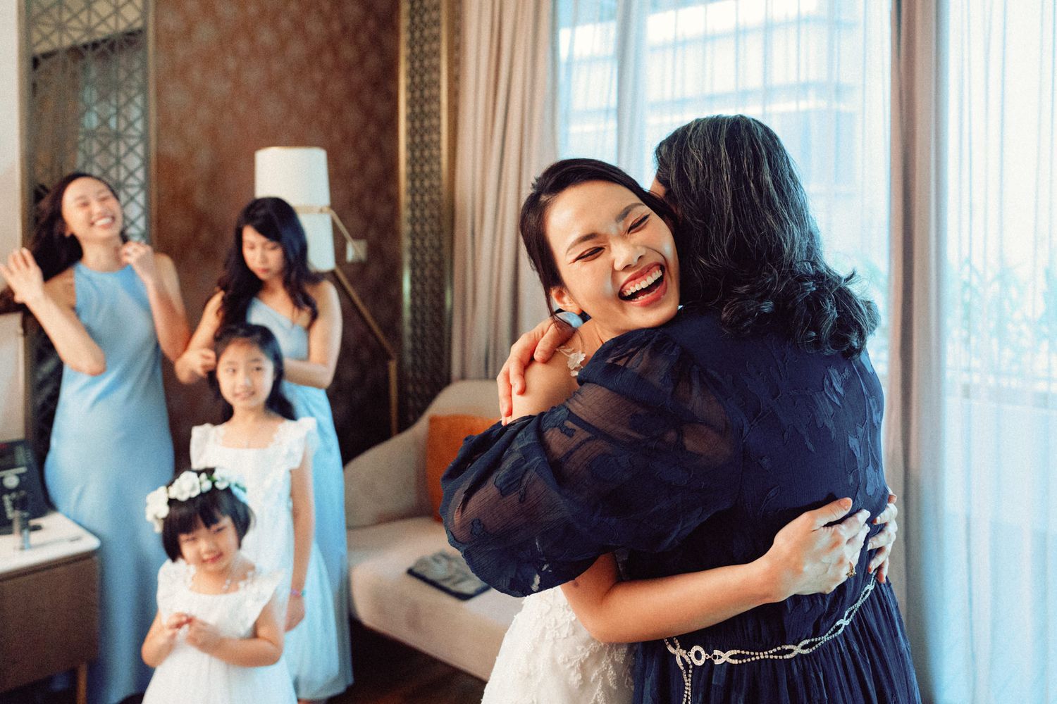 Bridesmaids in powder blue dresses assisting with wedding day preparations in an elegant hotel suite.