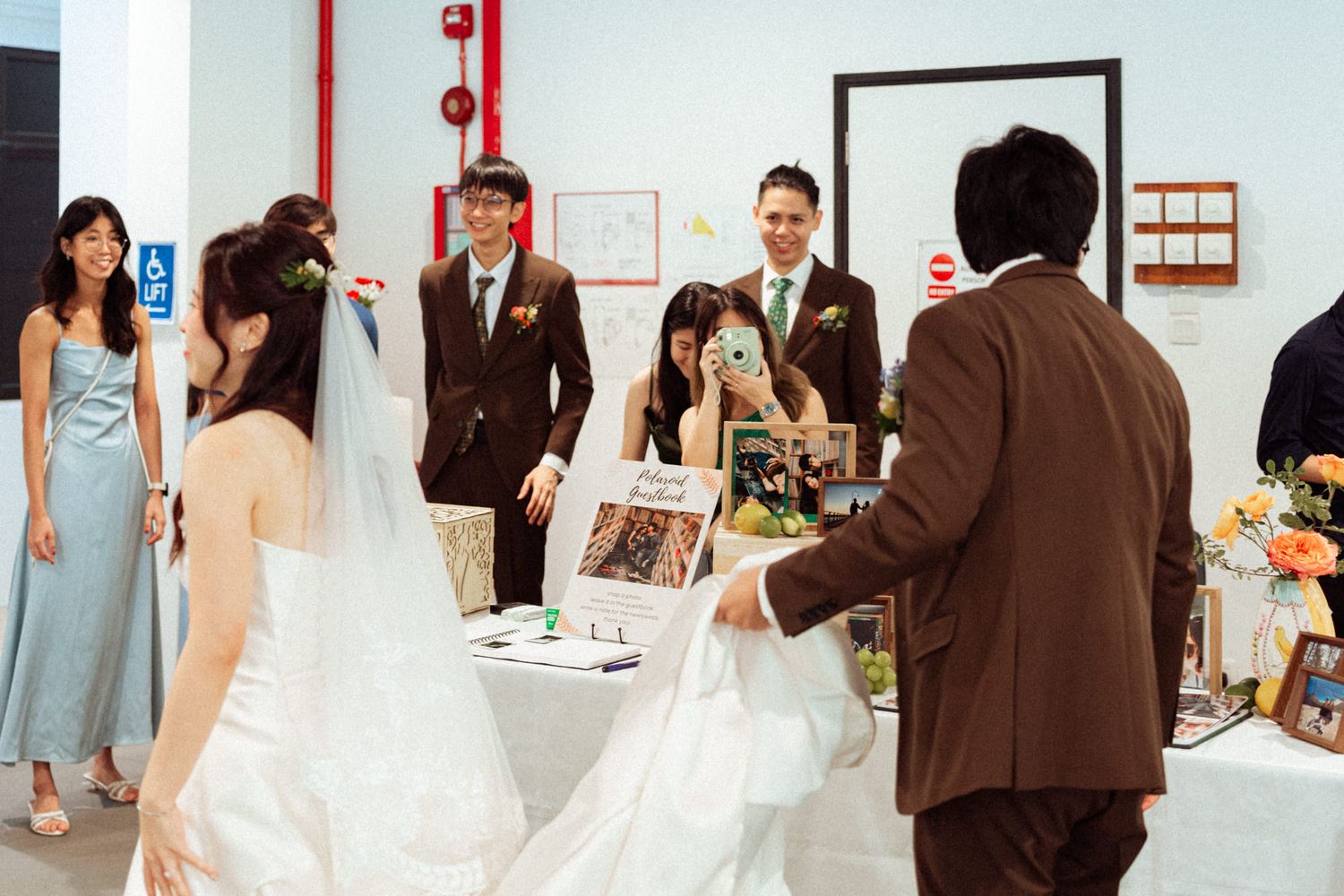 Wedding party gathering indoors, bride in white gown with guests and groomsmen in brown suits celebrating.