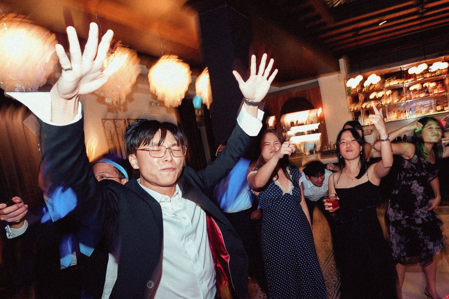 A group of people dancing and celebrating at a festive indoor party with paper lantern decorations.