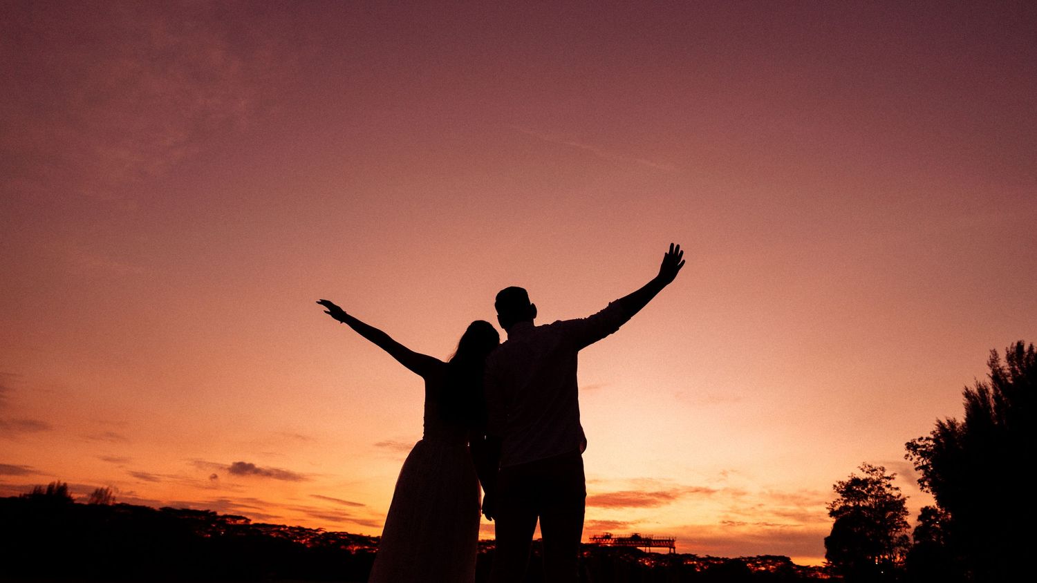 Silhouettes of people with raised arms stand against a dramatic orange and purple sunset sky.
