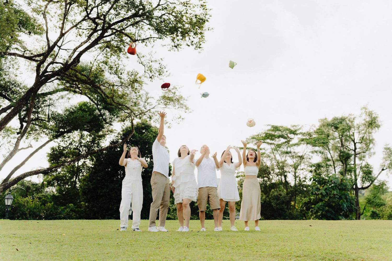 People in white outfits release colorful balloons into the sky during an outdoor celebration in a grassy field.