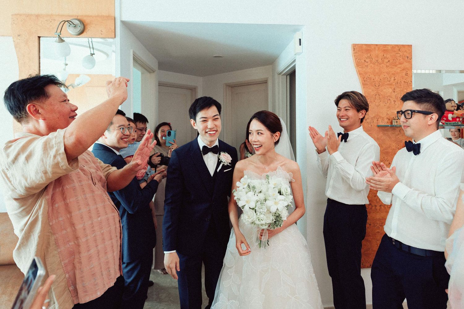 Wedding party celebrates with joyful poses and gestures in an indoor venue.