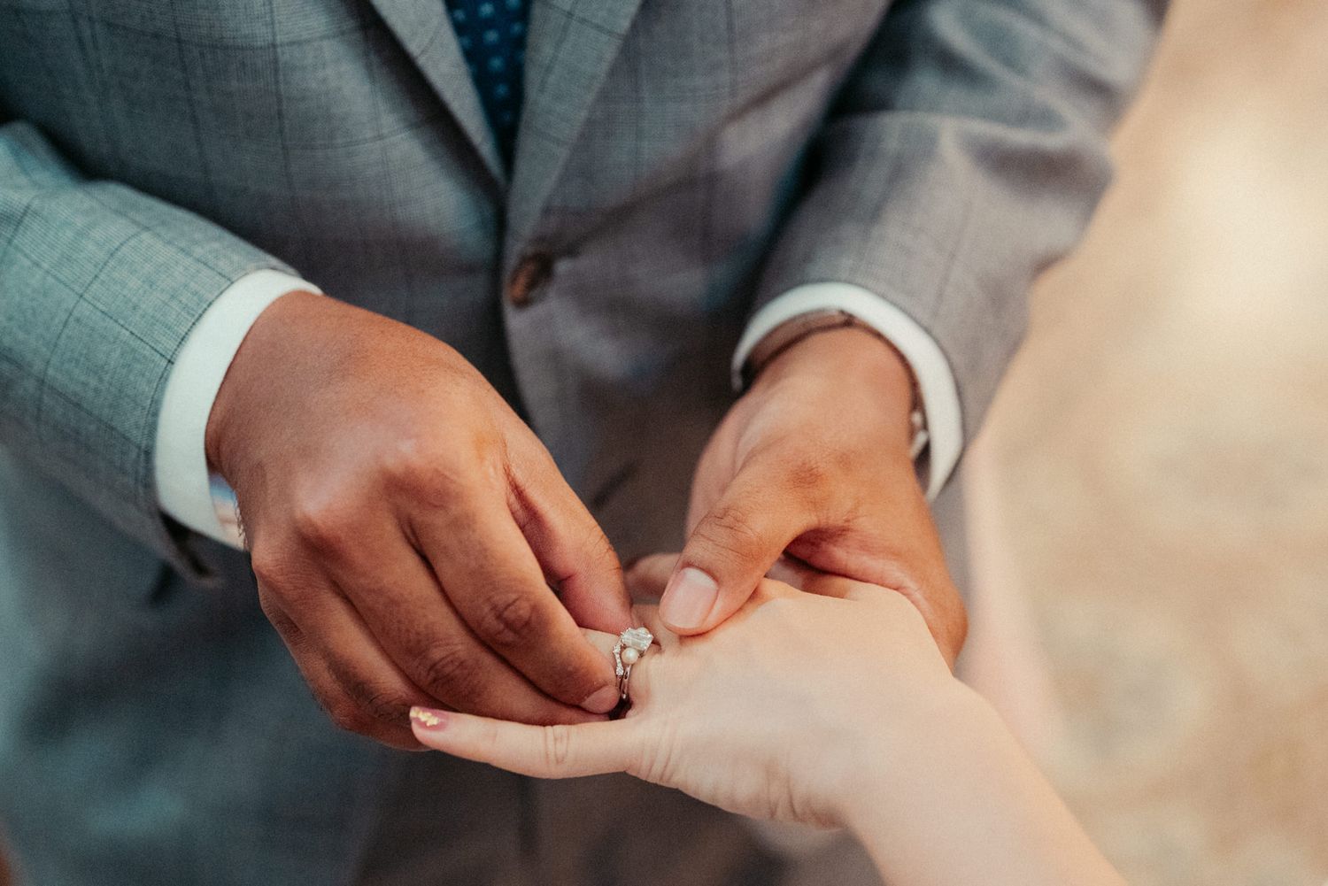 Groom placing a diamond engagement ring on bride's finger during wedding ceremony.