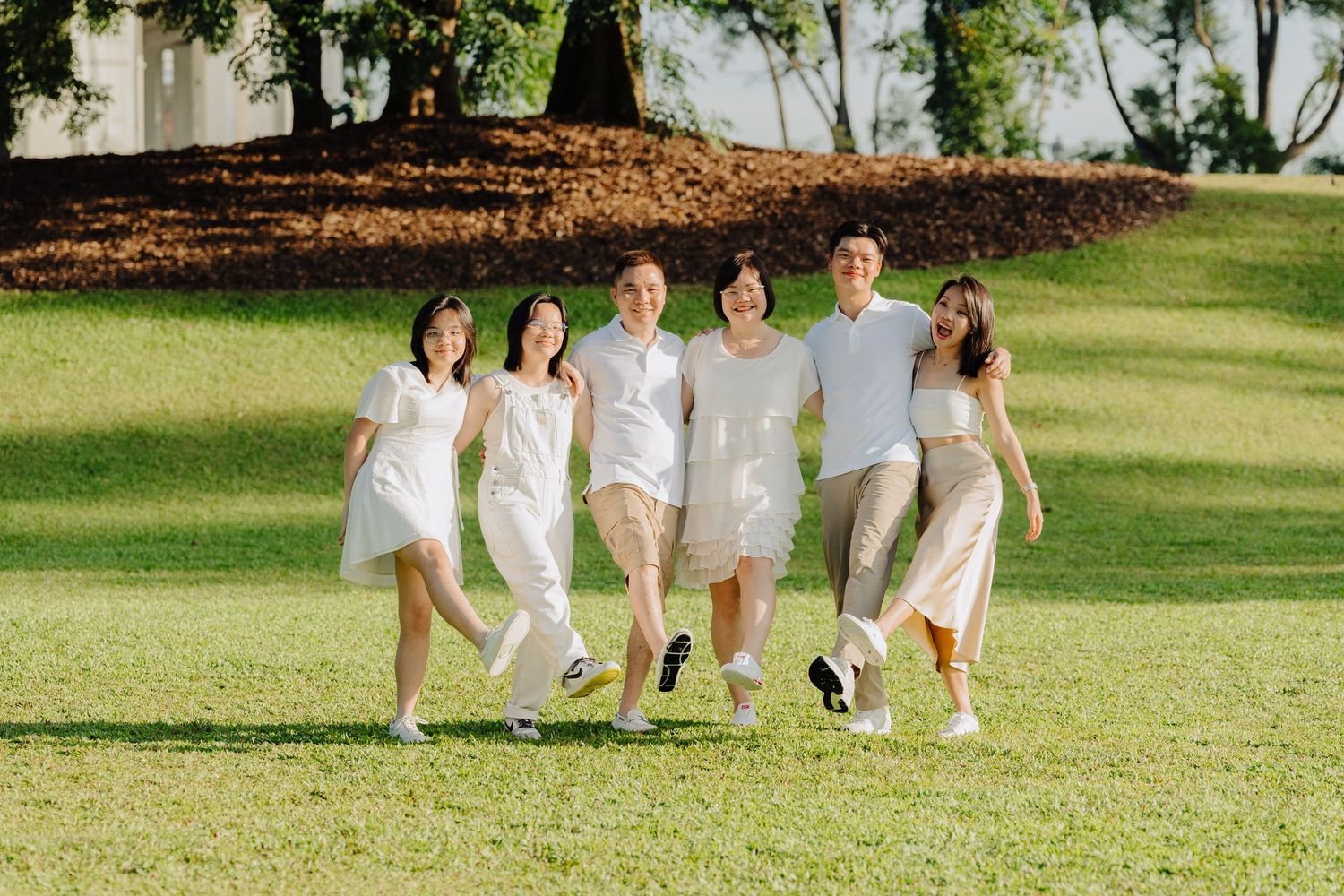 Group in white dresses walking and laughing together on a grassy lawn in the sunlight.