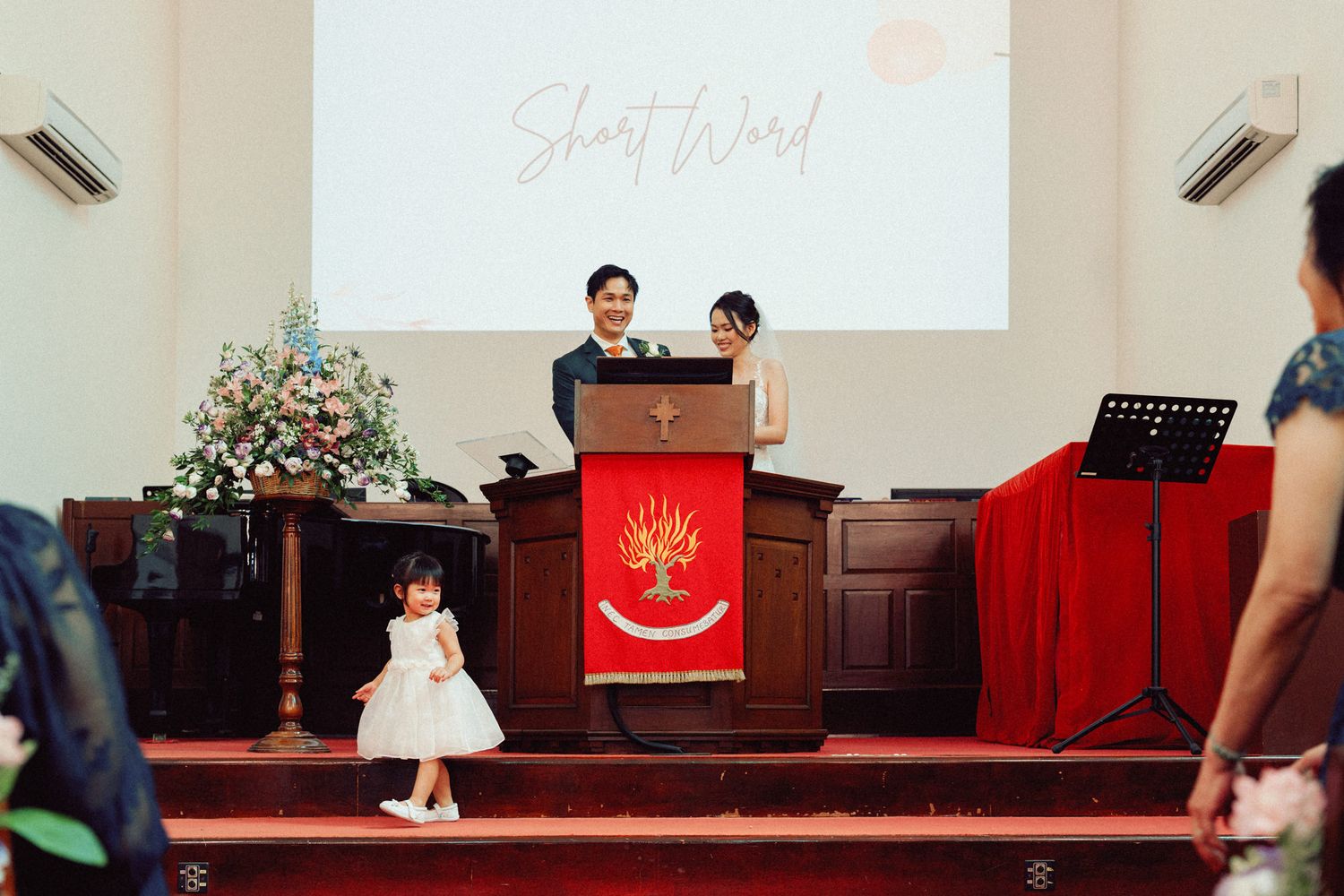 Wedding ceremony in progress at church altar with projection screen visible.
