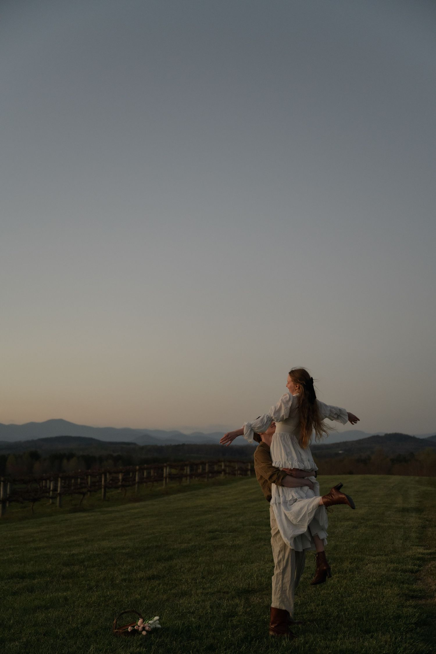 Couple dancing in an open field at sunset with mountains in the background.