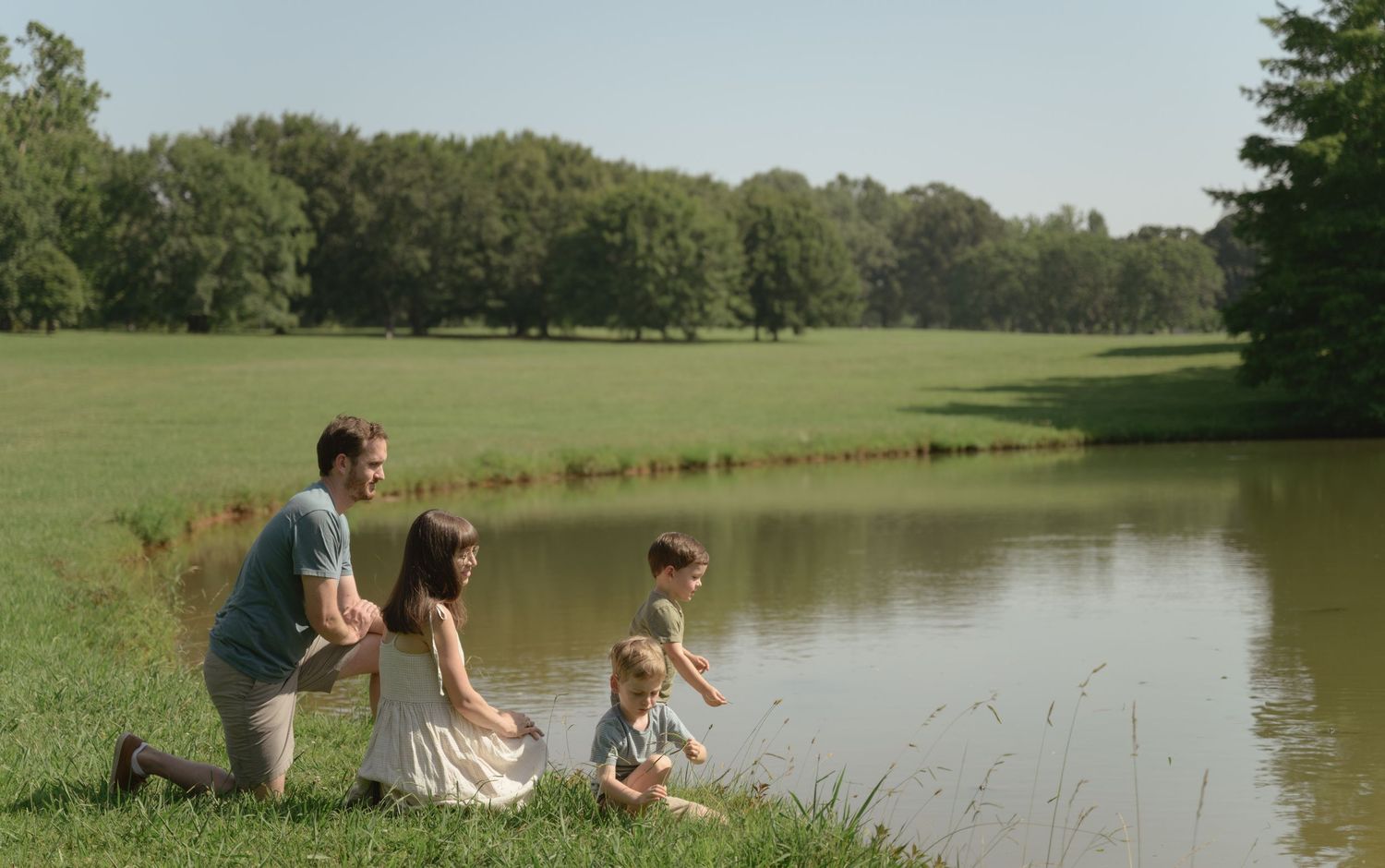 Family sitting by a peaceful pond on a summer day watching the water.