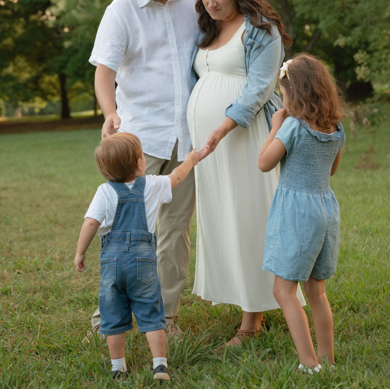 Family in coordinated denim and white outfits standing together in a sunny park.