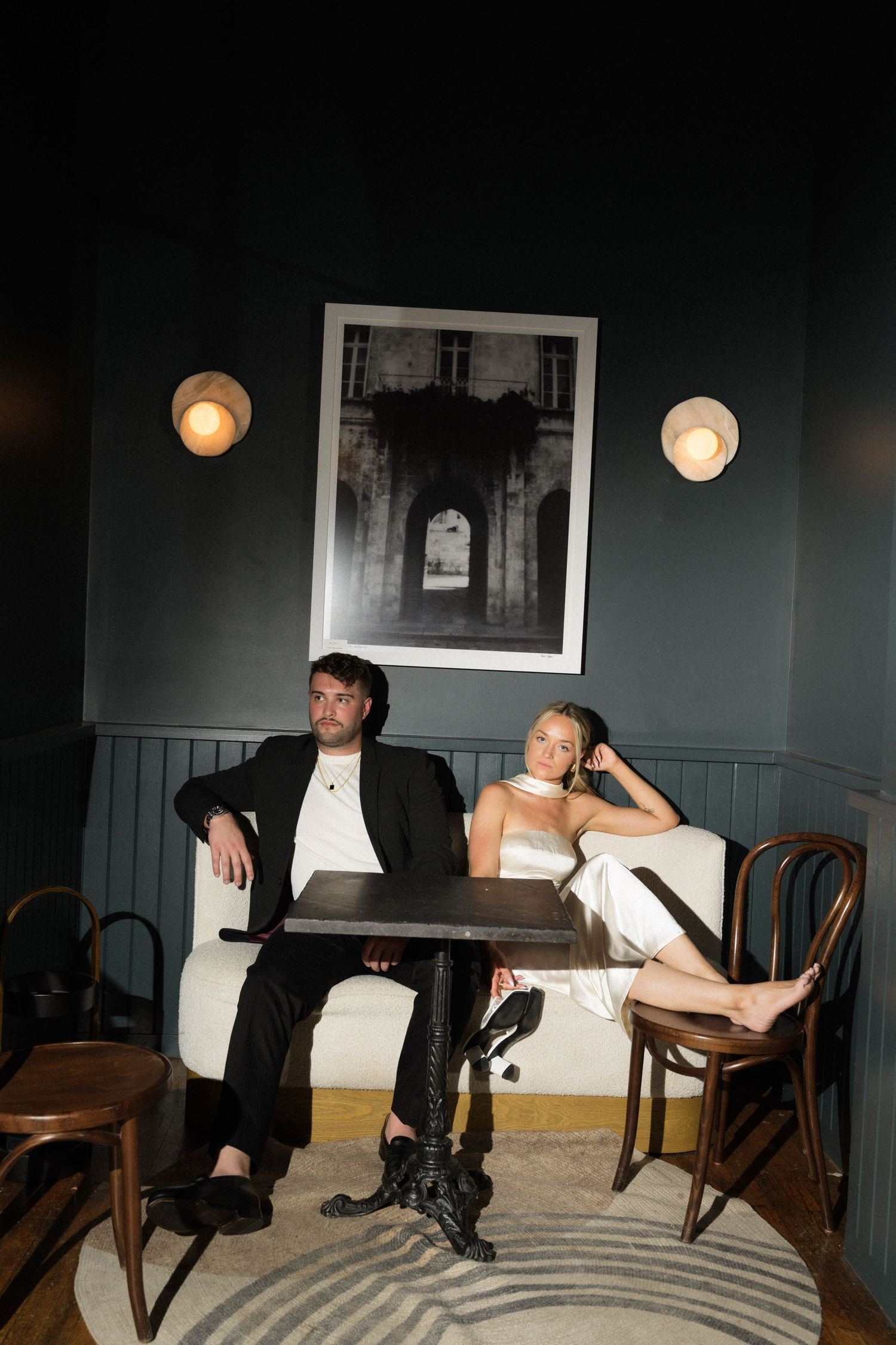 Stylish couple relaxing at bistro table in moody restaurant setting with wall art.