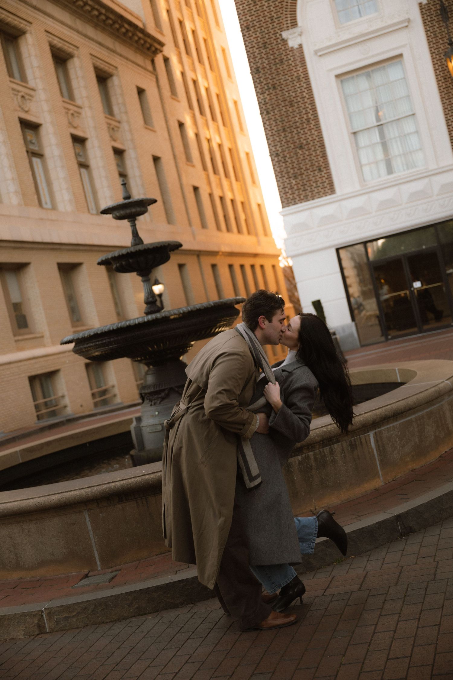 A photographer crouches low to capture an artistic angle on a brick sidewalk near a historic building facade.