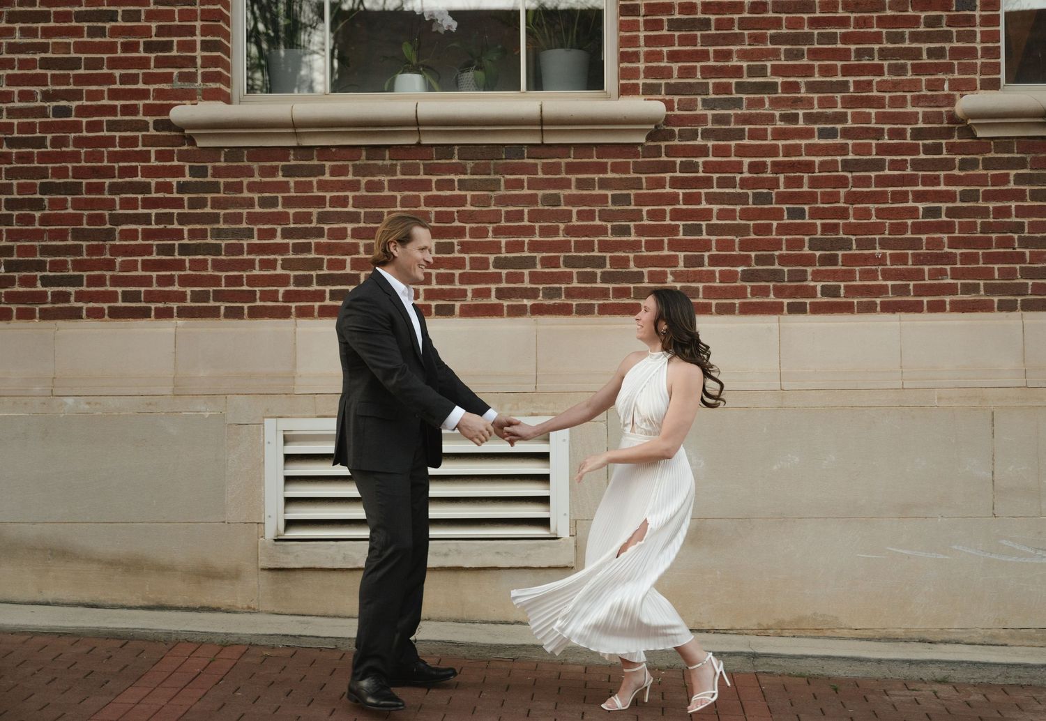 A couple dancing and twirling outside a brick building on a sunny day.