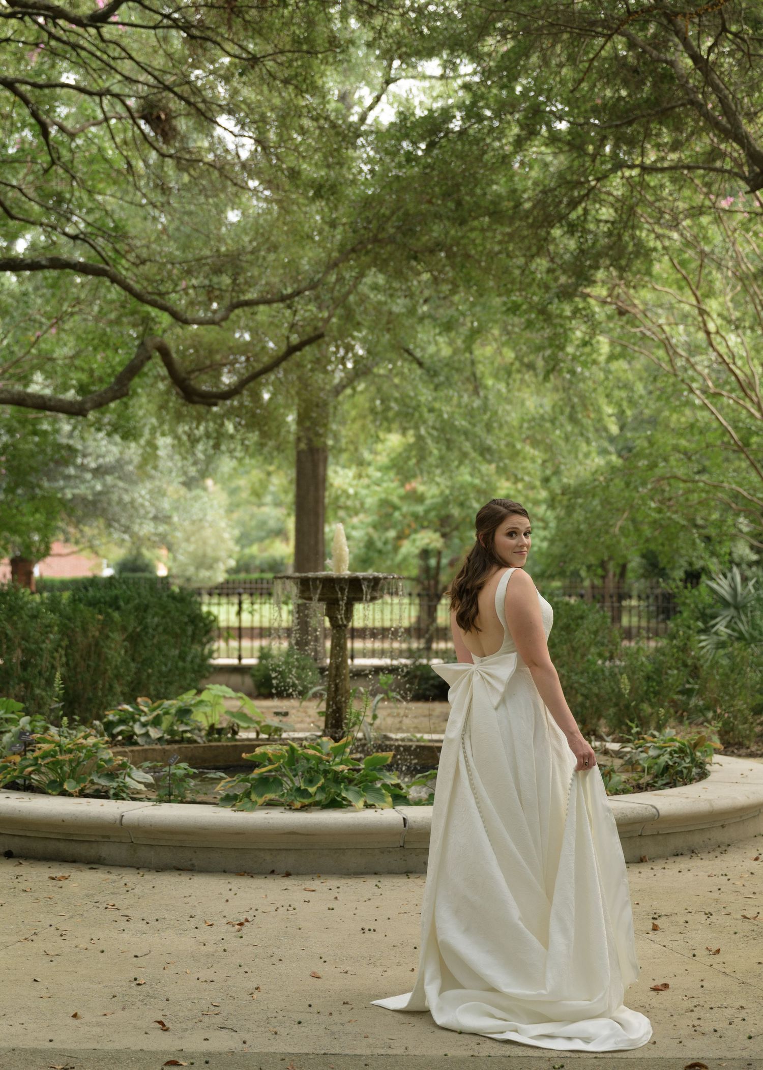 A white wedding dress flows elegantly across a garden pathway surrounded by lush greenery.