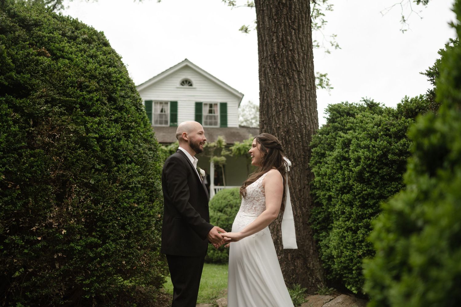 Romantic wedding couple embraces in a lush garden setting with greenery and trees in the background.