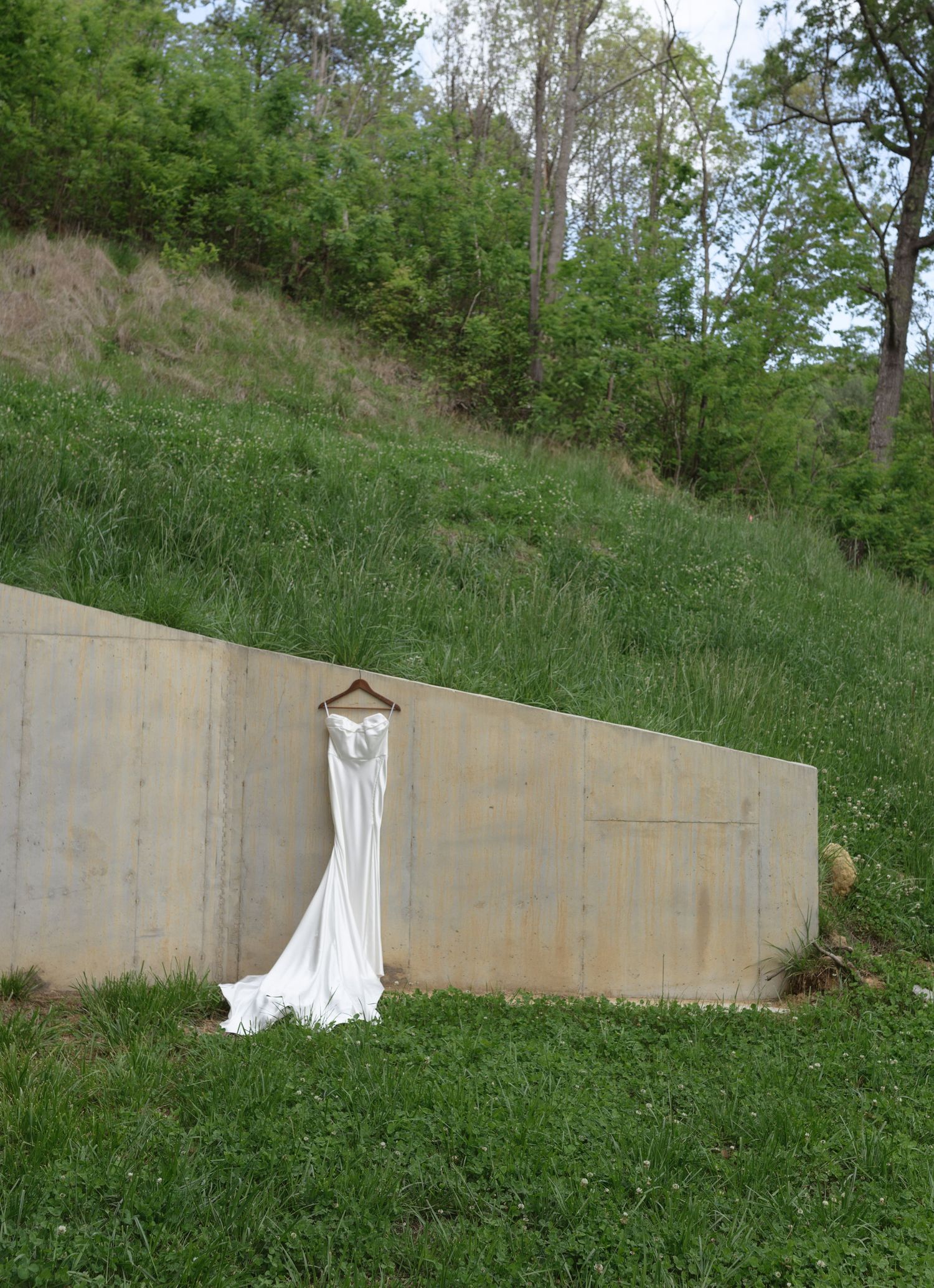 Wedding dress displayed against concrete wall in outdoor garden setting.