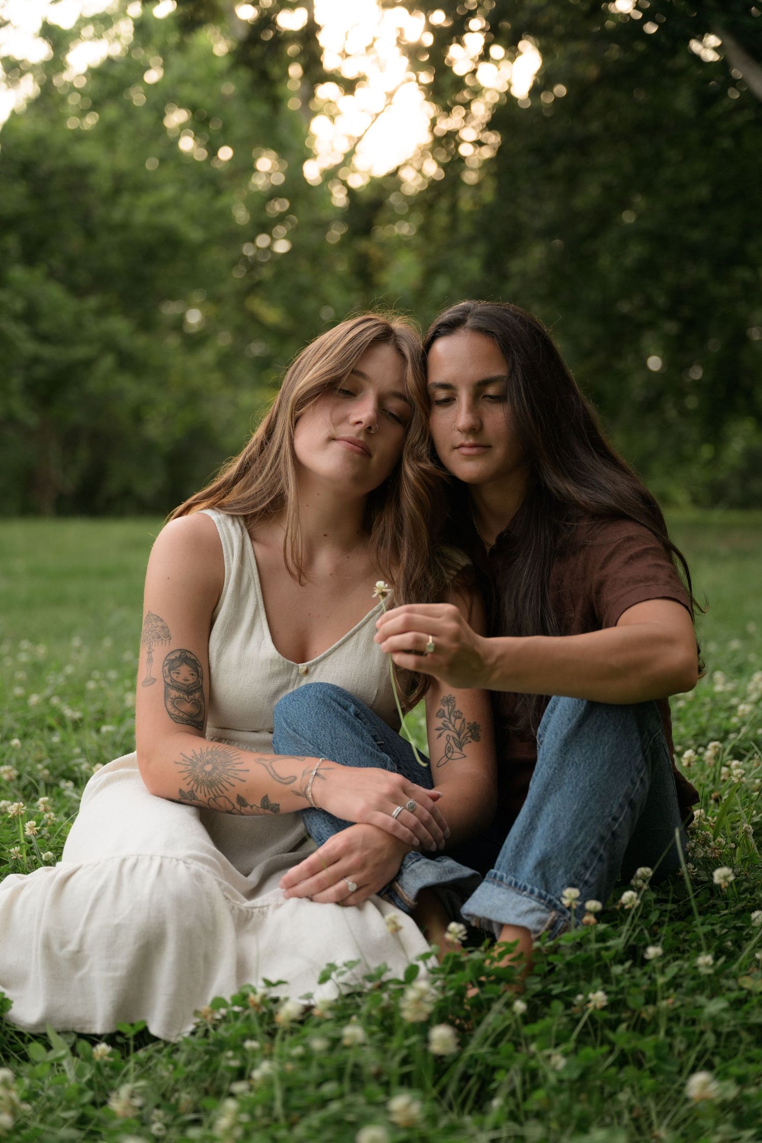 Two people relaxing together in a grassy meadow with white flowers during golden hour.