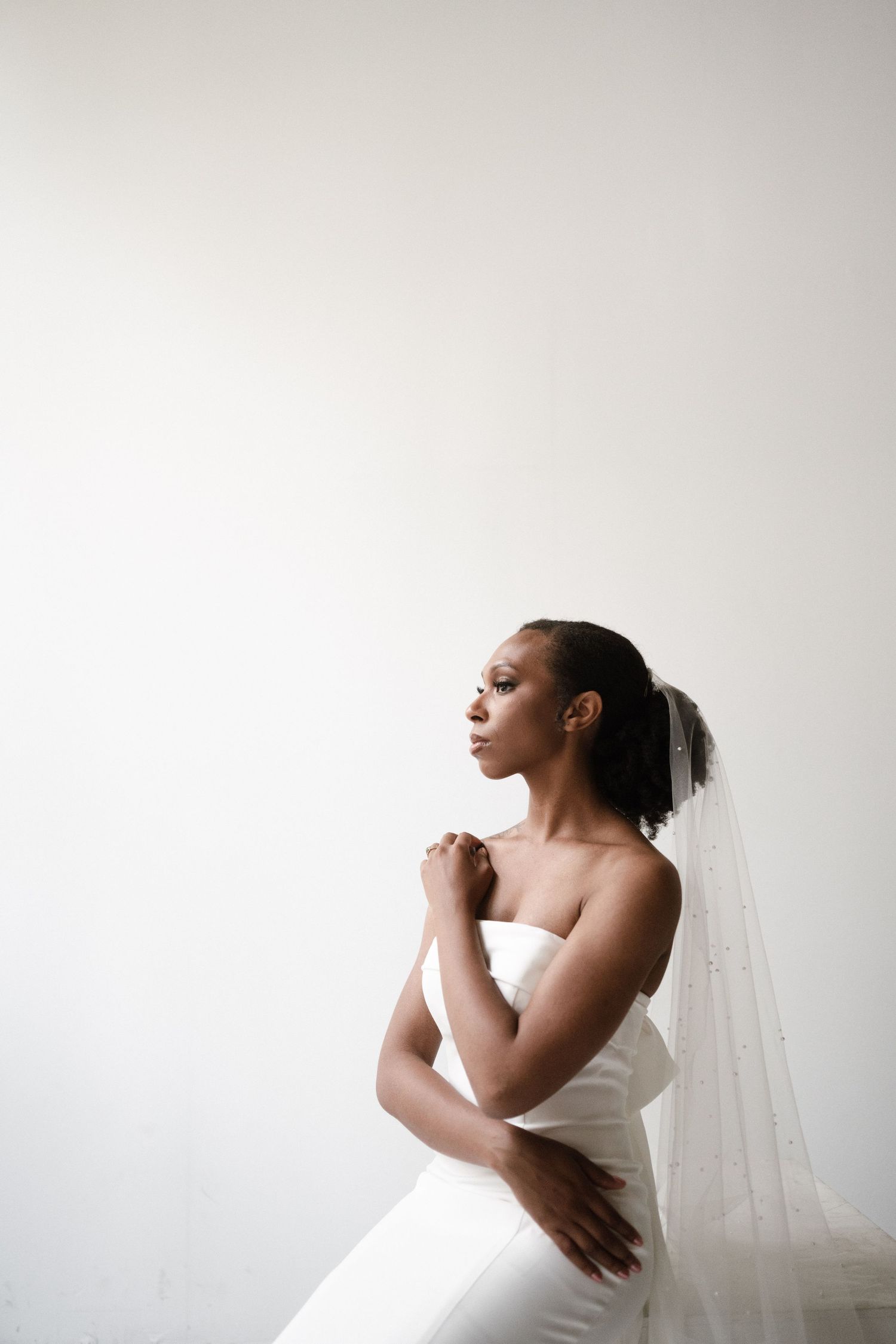 A bride in a flowing white gown poses gracefully against a minimalist white backdrop.