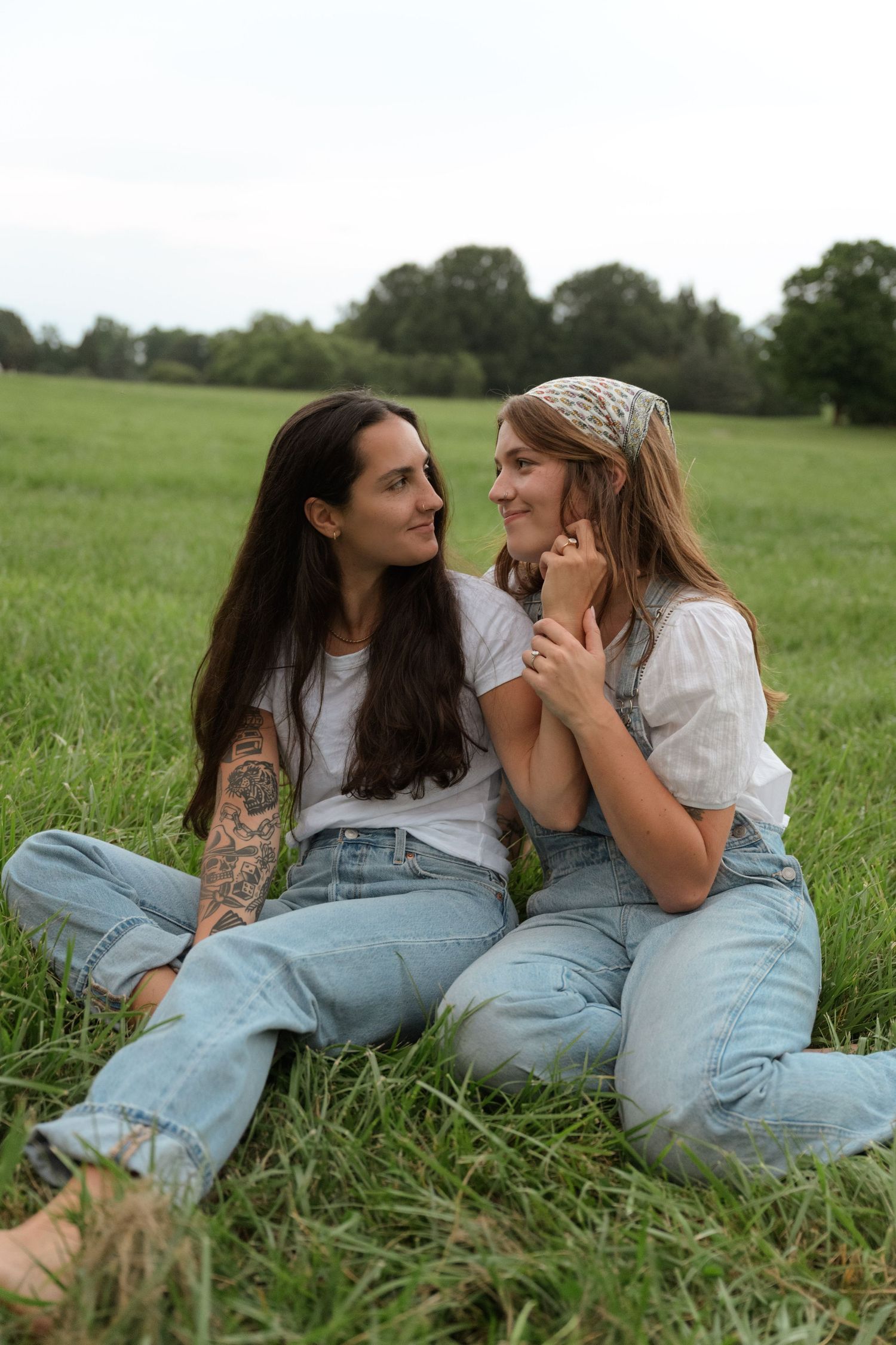 Two people in casual denim lying close together in grassy summer field.