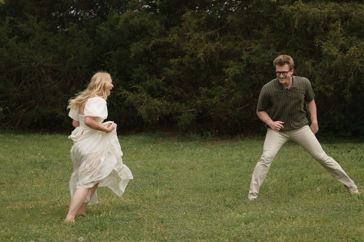 Couple in coordinated outfits playing and running together in a grassy field.